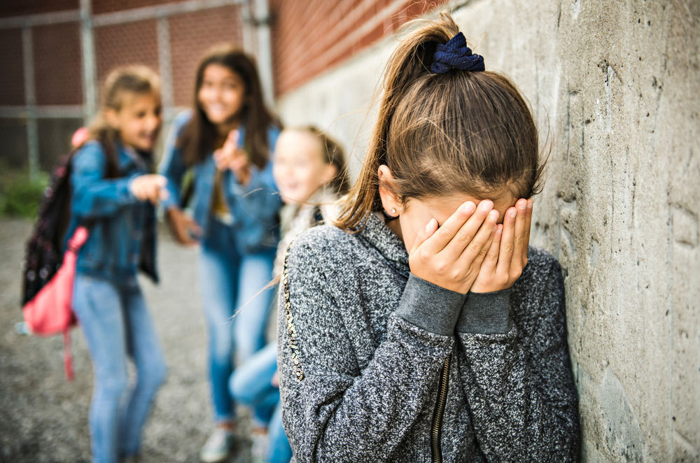 child with head in hands with other girls laughing at her
