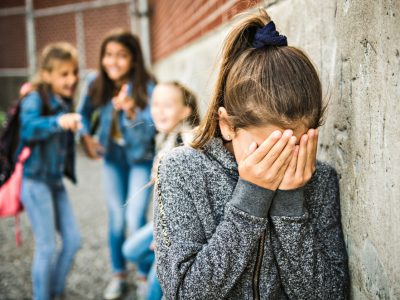 child with head in hands with other girls laughing at her